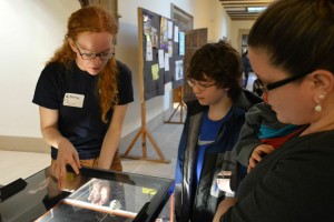 Undergraduate volunteer Emma Graham shows attendees an apparatus that detects ionizing radiation. Photo by Suryabrata Dutta.